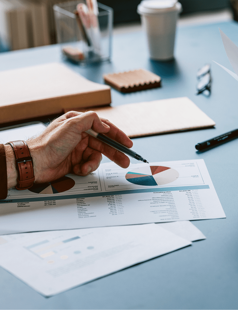 Hand pointing at financial charts on desk.