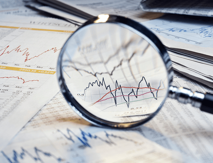 Magnifying glass over financial charts and graphs.